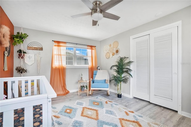 bedroom with a nursery area, a closet, light hardwood / wood-style flooring, and ceiling fan