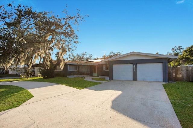 ranch-style home featuring a garage, a front yard, concrete driveway, and fence