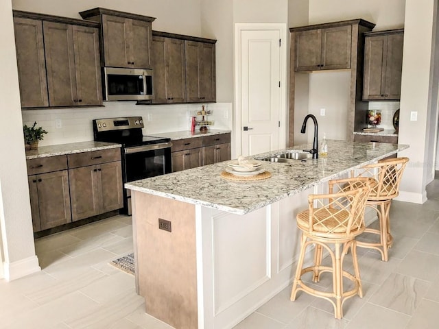 kitchen with sink, an island with sink, stainless steel appliances, backsplash, and light stone countertops