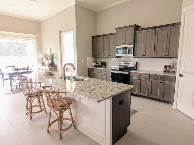 kitchen with a breakfast bar, light stone counters, sink, a center island with sink, and appliances with stainless steel finishes