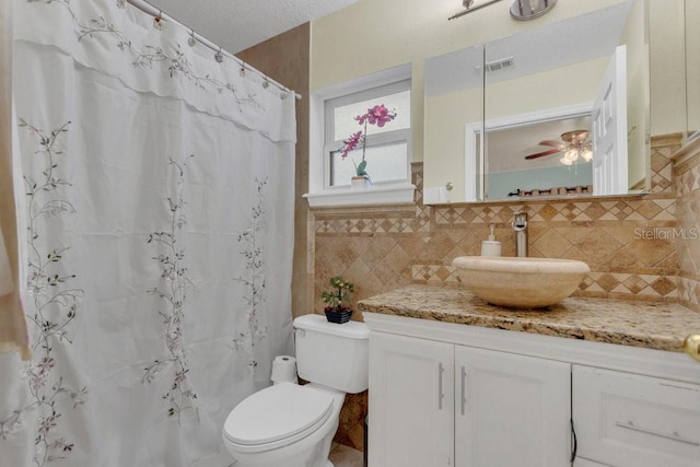 bathroom featuring ceiling fan, vanity, a textured ceiling, tile walls, and toilet