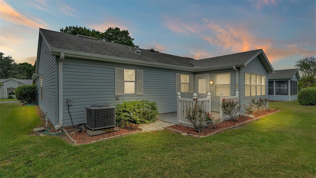 view of front of property featuring central AC, a sunroom, and a lawn