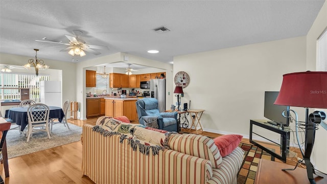 living room with ceiling fan with notable chandelier, a textured ceiling, and light hardwood / wood-style floors