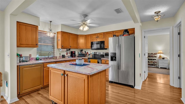 kitchen with a kitchen island, sink, hanging light fixtures, stainless steel appliances, and light wood-type flooring