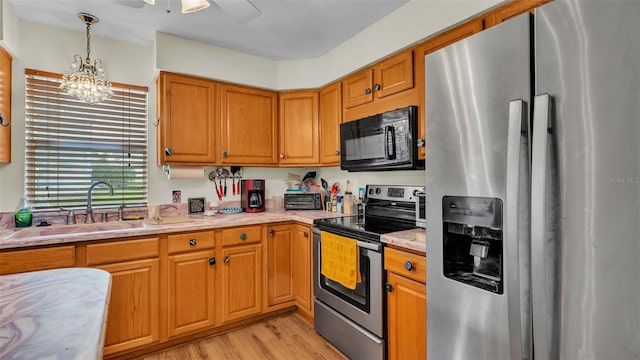 kitchen with sink, ceiling fan with notable chandelier, appliances with stainless steel finishes, decorative light fixtures, and light wood-type flooring