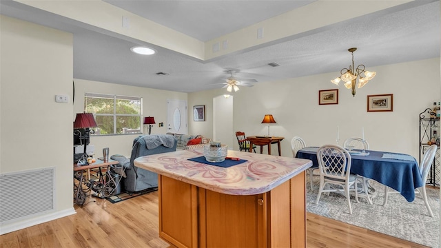 kitchen featuring ceiling fan with notable chandelier, light hardwood / wood-style floors, a textured ceiling, and pendant lighting