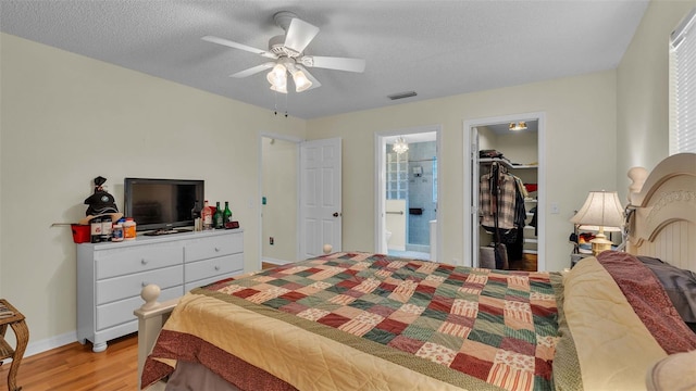 bedroom featuring ceiling fan, a textured ceiling, a walk in closet, a closet, and light wood-type flooring