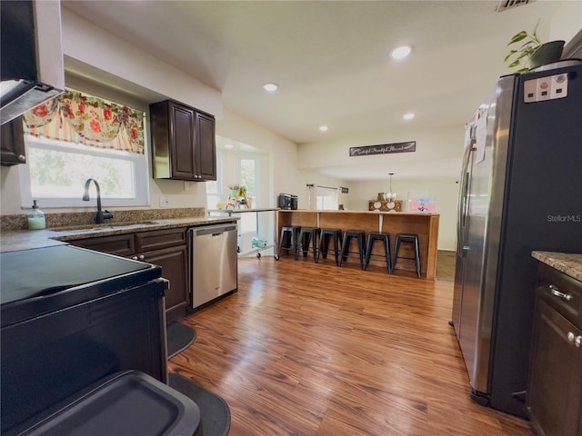 kitchen featuring light hardwood / wood-style floors, sink, hanging light fixtures, appliances with stainless steel finishes, and dark brown cabinetry