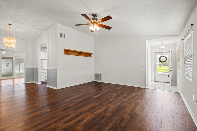 unfurnished living room with a textured ceiling, a wealth of natural light, vaulted ceiling, and dark hardwood / wood-style flooring