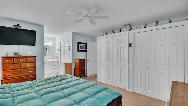 carpeted bedroom featuring a textured ceiling, connected bathroom, two closets, and ceiling fan