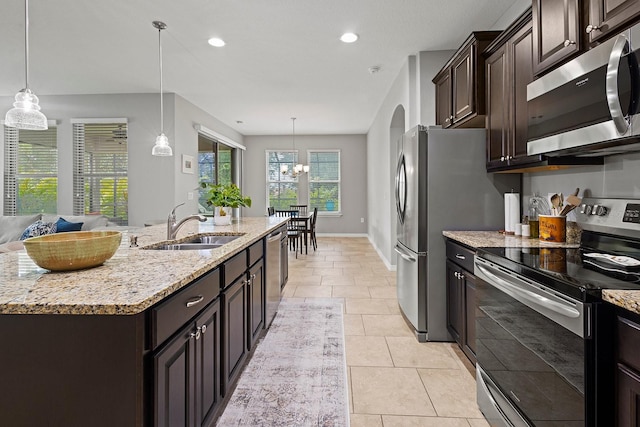 kitchen with sink, appliances with stainless steel finishes, a kitchen island with sink, hanging light fixtures, and dark brown cabinetry