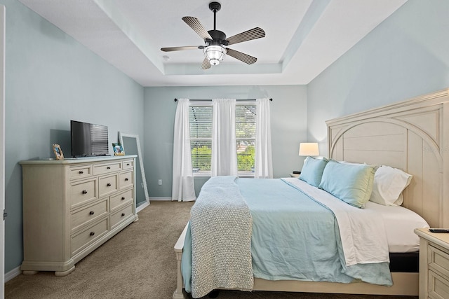 carpeted bedroom with ceiling fan and a raised ceiling