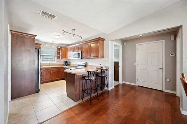 kitchen with sink, kitchen peninsula, light hardwood / wood-style flooring, stainless steel appliances, and a breakfast bar