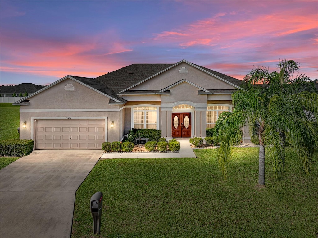 ranch-style home featuring an attached garage, a front yard, concrete driveway, and stucco siding