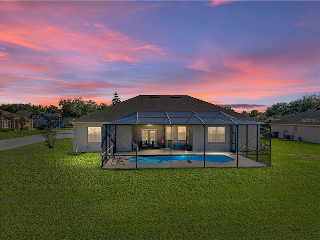 back house at dusk featuring a yard, a patio area, and a lanai