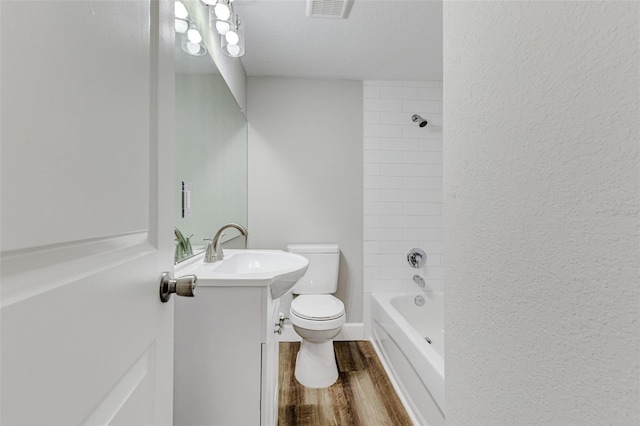 full bathroom featuring vanity, tiled shower / bath combo, wood-type flooring, a textured ceiling, and toilet