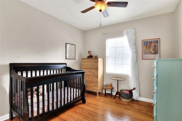 bedroom featuring ceiling fan, a crib, wood finished floors, and baseboards