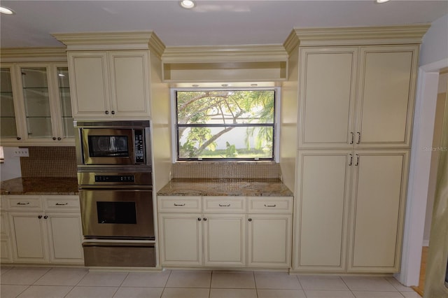 kitchen featuring backsplash, dark stone countertops, cream cabinetry, and stainless steel appliances