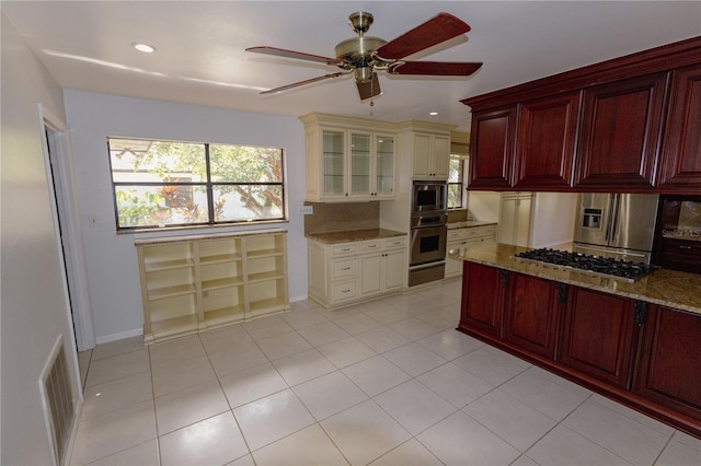 kitchen featuring appliances with stainless steel finishes, light tile patterned flooring, light stone countertops, and ceiling fan