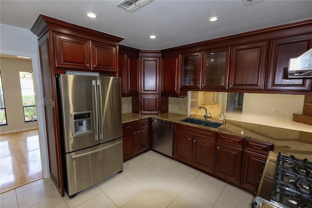 kitchen with range hood, sink, backsplash, stone counters, and appliances with stainless steel finishes