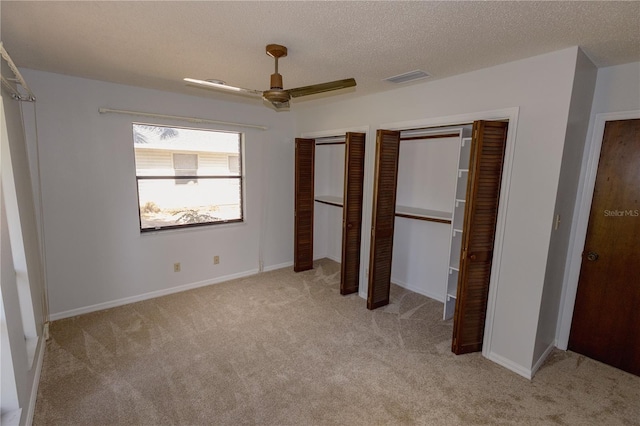 unfurnished bedroom with a textured ceiling, ceiling fan, light colored carpet, and two closets