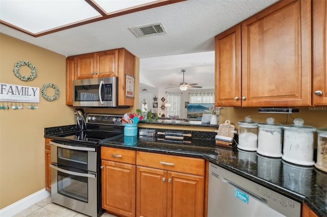 kitchen featuring a textured ceiling, stainless steel appliances, ceiling fan, light tile patterned floors, and dark stone countertops