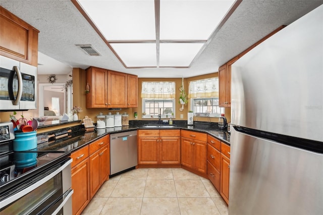 kitchen with a textured ceiling, dark stone countertops, sink, and stainless steel appliances