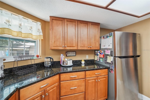 kitchen featuring stainless steel refrigerator, dark stone countertops, and a textured ceiling