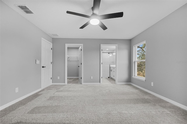 unfurnished bedroom with ceiling fan, light colored carpet, a spacious closet, and connected bathroom