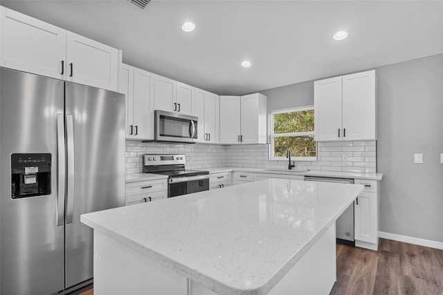 kitchen with appliances with stainless steel finishes, dark wood-type flooring, sink, white cabinets, and a kitchen island