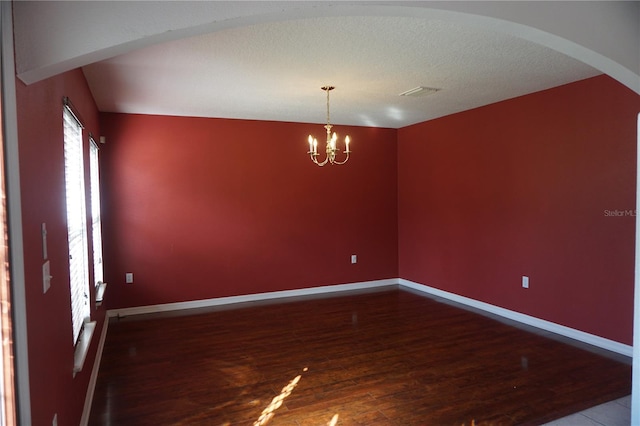 empty room featuring a textured ceiling, wood-type flooring, lofted ceiling, and a chandelier