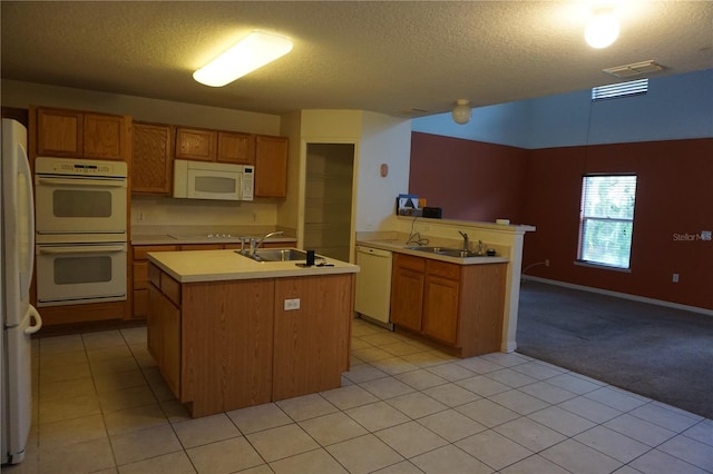 kitchen featuring white appliances, kitchen peninsula, a textured ceiling, a kitchen island with sink, and sink