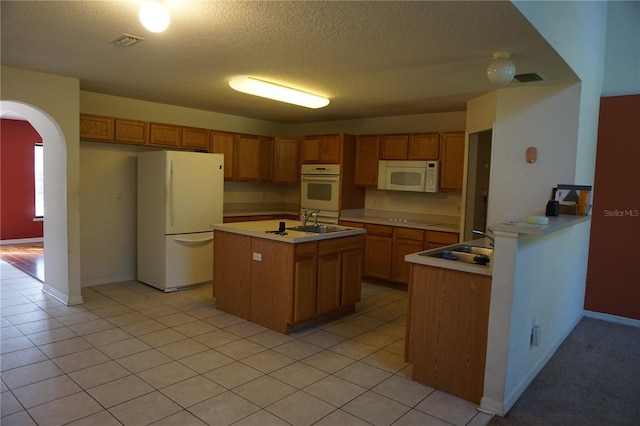 kitchen with white appliances, a center island with sink, light tile patterned flooring, and a textured ceiling