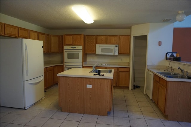 kitchen with a textured ceiling, white appliances, light tile patterned flooring, and sink