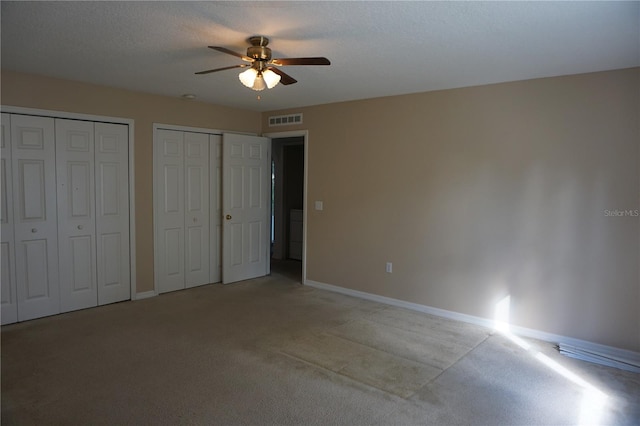 unfurnished bedroom featuring ceiling fan, multiple closets, a textured ceiling, and light colored carpet