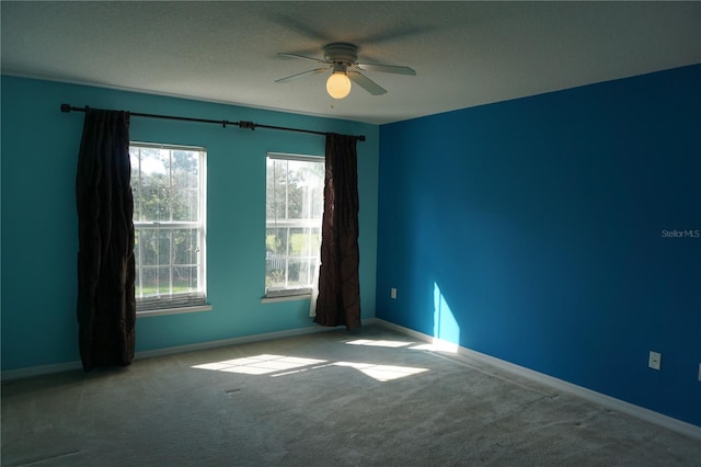 empty room featuring ceiling fan, light colored carpet, a textured ceiling, and a healthy amount of sunlight