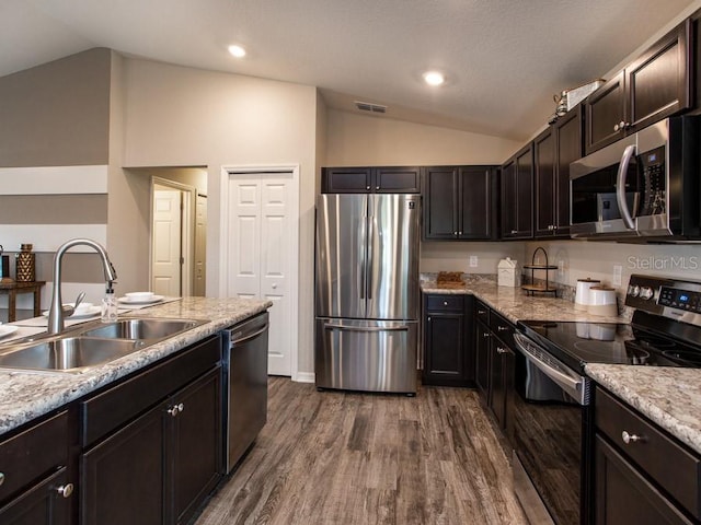 kitchen featuring light stone counters, hardwood / wood-style flooring, sink, vaulted ceiling, and appliances with stainless steel finishes