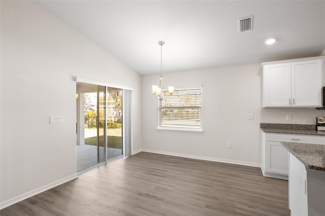 unfurnished dining area featuring dark hardwood / wood-style floors, vaulted ceiling, and a notable chandelier