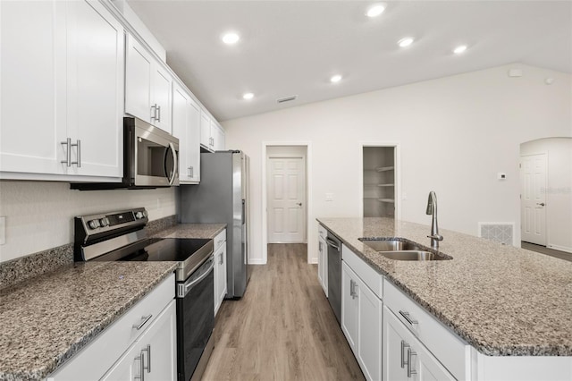 kitchen with sink, vaulted ceiling, appliances with stainless steel finishes, a kitchen island with sink, and white cabinets