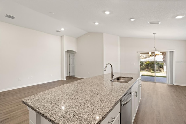 kitchen featuring decorative light fixtures, lofted ceiling, sink, white cabinets, and a kitchen island with sink