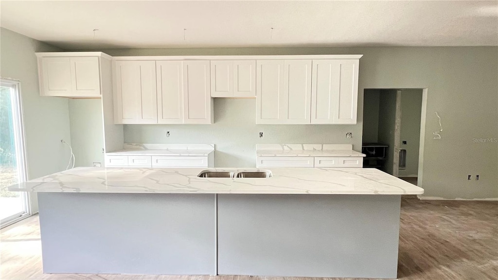 kitchen with an island with sink, light wood-type flooring, white cabinetry, and light stone countertops