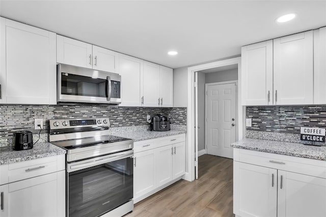 kitchen with light stone counters, white cabinets, light hardwood / wood-style flooring, backsplash, and stainless steel appliances