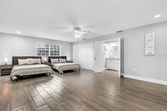 bedroom featuring ceiling fan, a textured ceiling, a closet, ensuite bath, and hardwood / wood-style floors