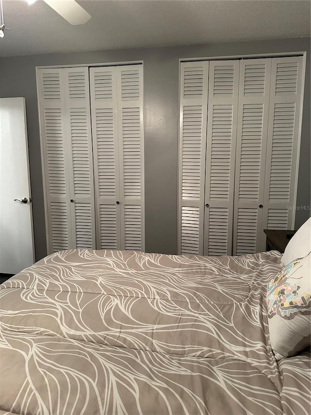 bedroom featuring ceiling fan, a textured ceiling, and two closets