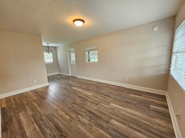 unfurnished room with an inviting chandelier, dark hardwood / wood-style flooring, and a textured ceiling