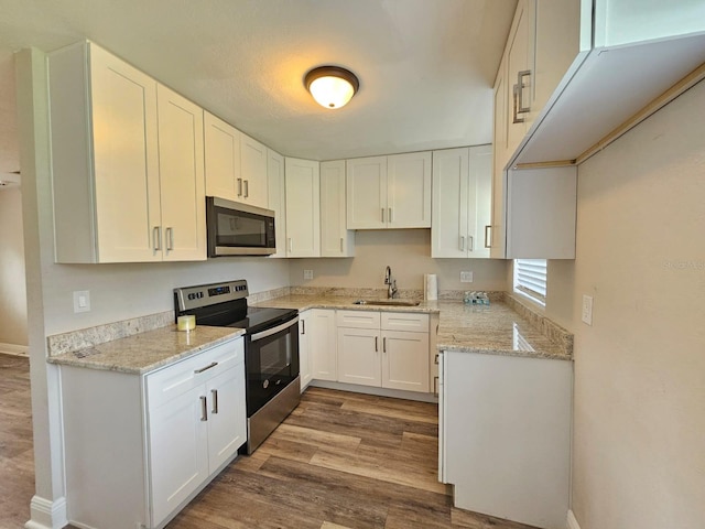 kitchen with sink, wood-type flooring, white cabinetry, stainless steel appliances, and light stone countertops