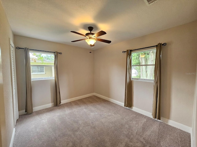 carpeted spare room featuring ceiling fan, a textured ceiling, and plenty of natural light