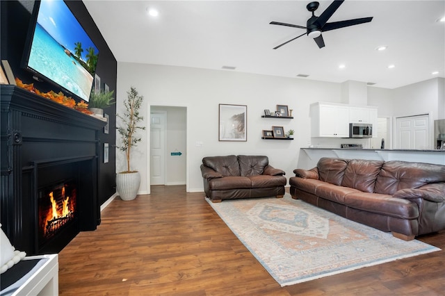 living room featuring a large fireplace, dark hardwood / wood-style floors, and ceiling fan