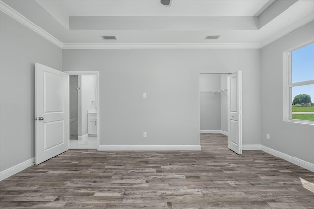 unfurnished bedroom featuring crown molding, wood-type flooring, a tray ceiling, and a walk in closet