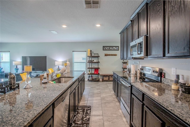 kitchen featuring sink, stainless steel appliances, light tile patterned floors, dark brown cabinetry, and dark stone countertops